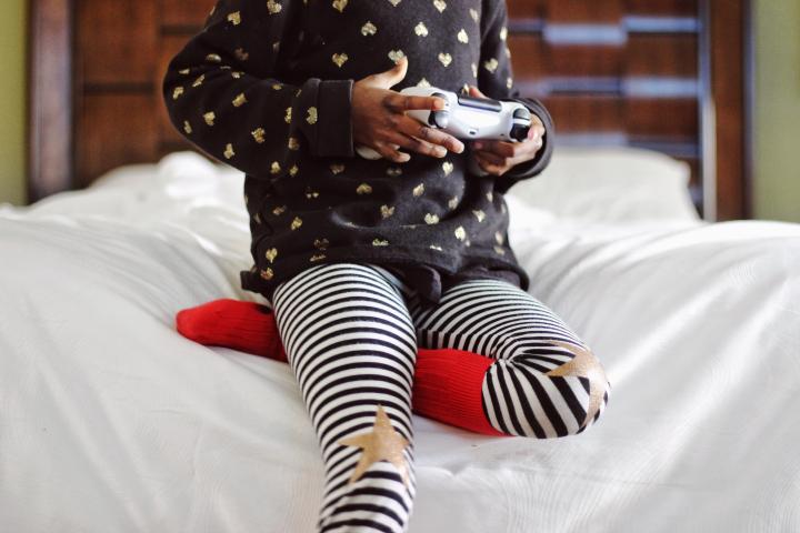 Titelbild pädagogische Chancen, kleines Mädchen halb auf Bett sitzend mit Controller in der Hand