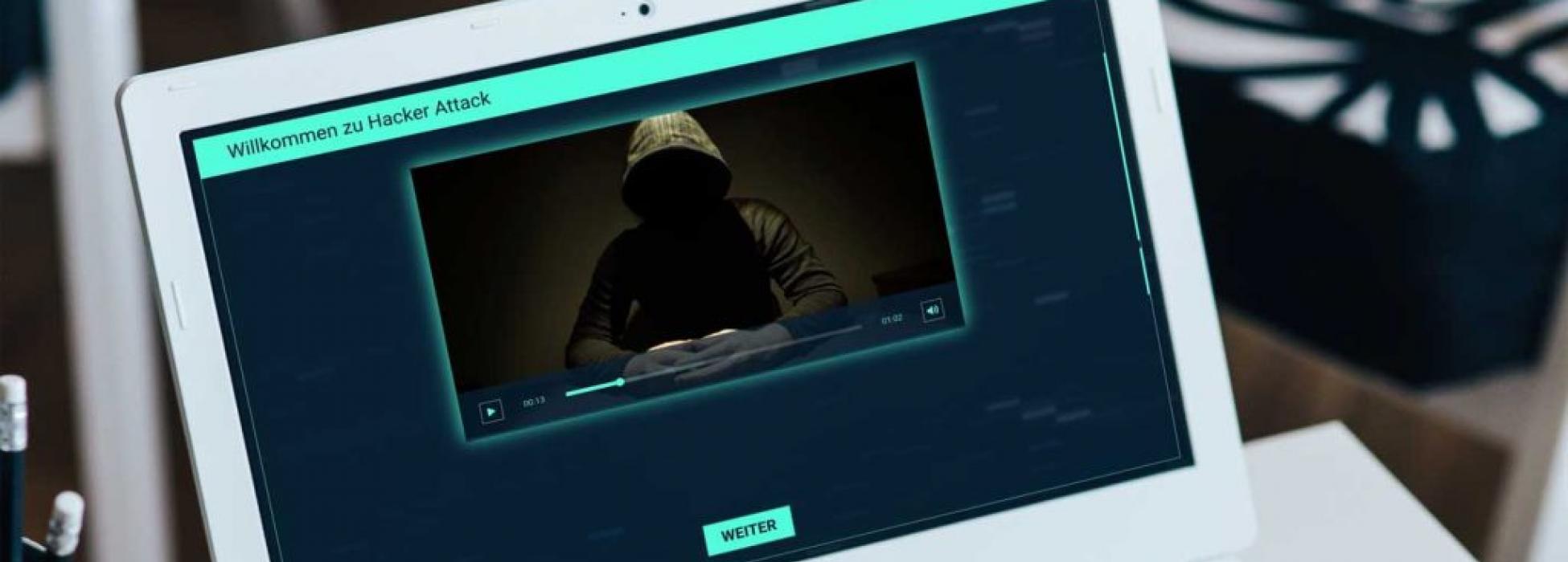 Ein Laptop zeigt einen Videoausschnitt mit einem vermummten Hacker aus dem digitalen Escape Room 'Hacker Attack'
